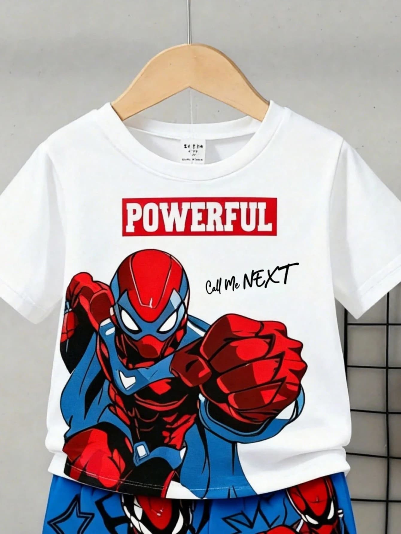Close-up of the kids' white T-shirt front, showing the red 'POWERFUL' box logo and a red-and-blue comic superhero graphic.