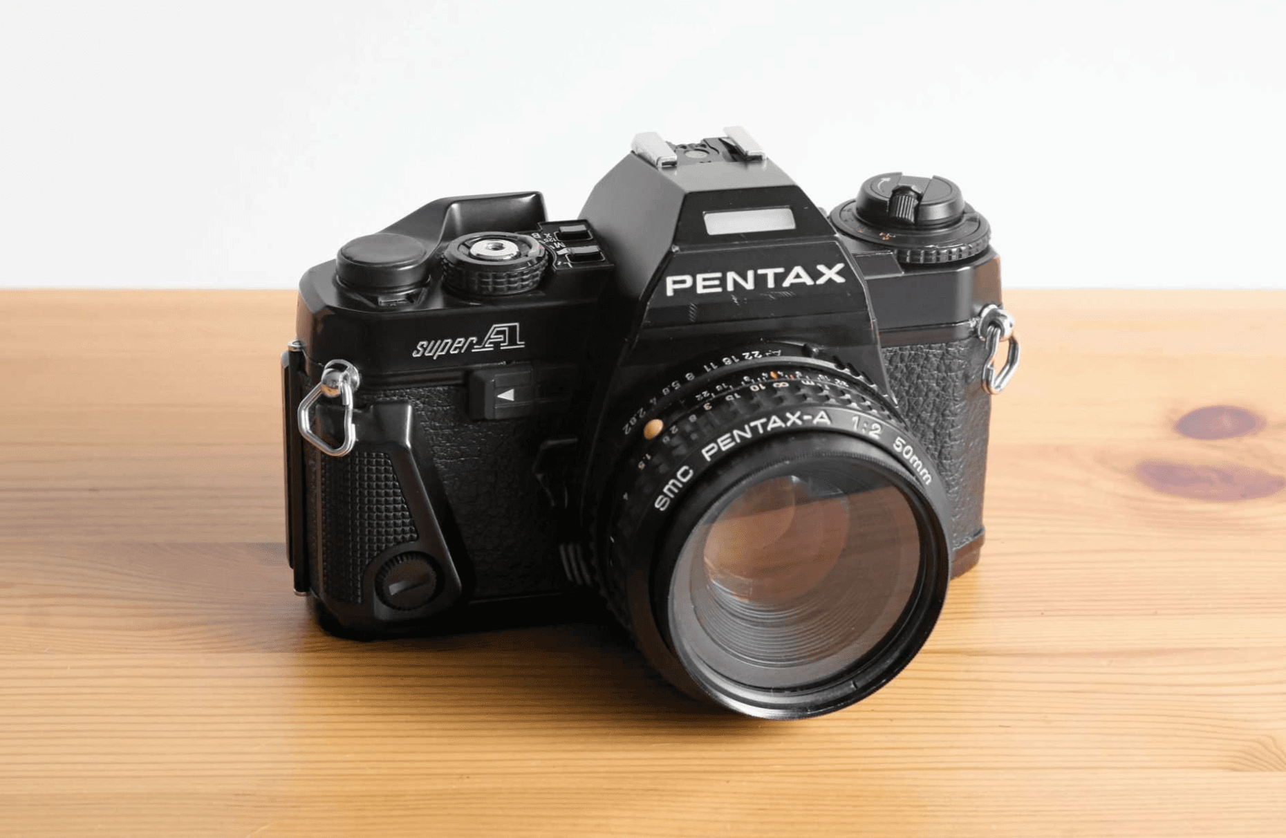Front view of a black Pentax Super A 35mm SLR film camera with a 50mm lens, on a wooden surface.