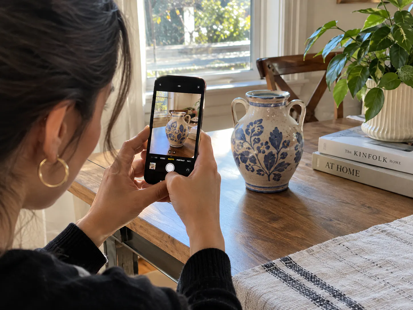 Frau fotografiert zu Hause mit ihrem Smartphone eine dekorative Keramikvase.